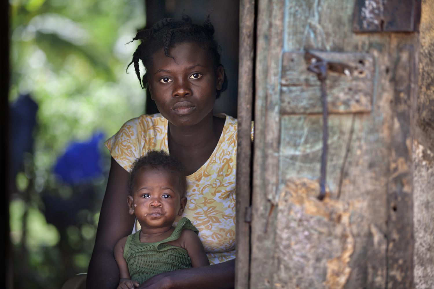 A woman and her baby sit in the doorway of their home in Milot, Haiti.